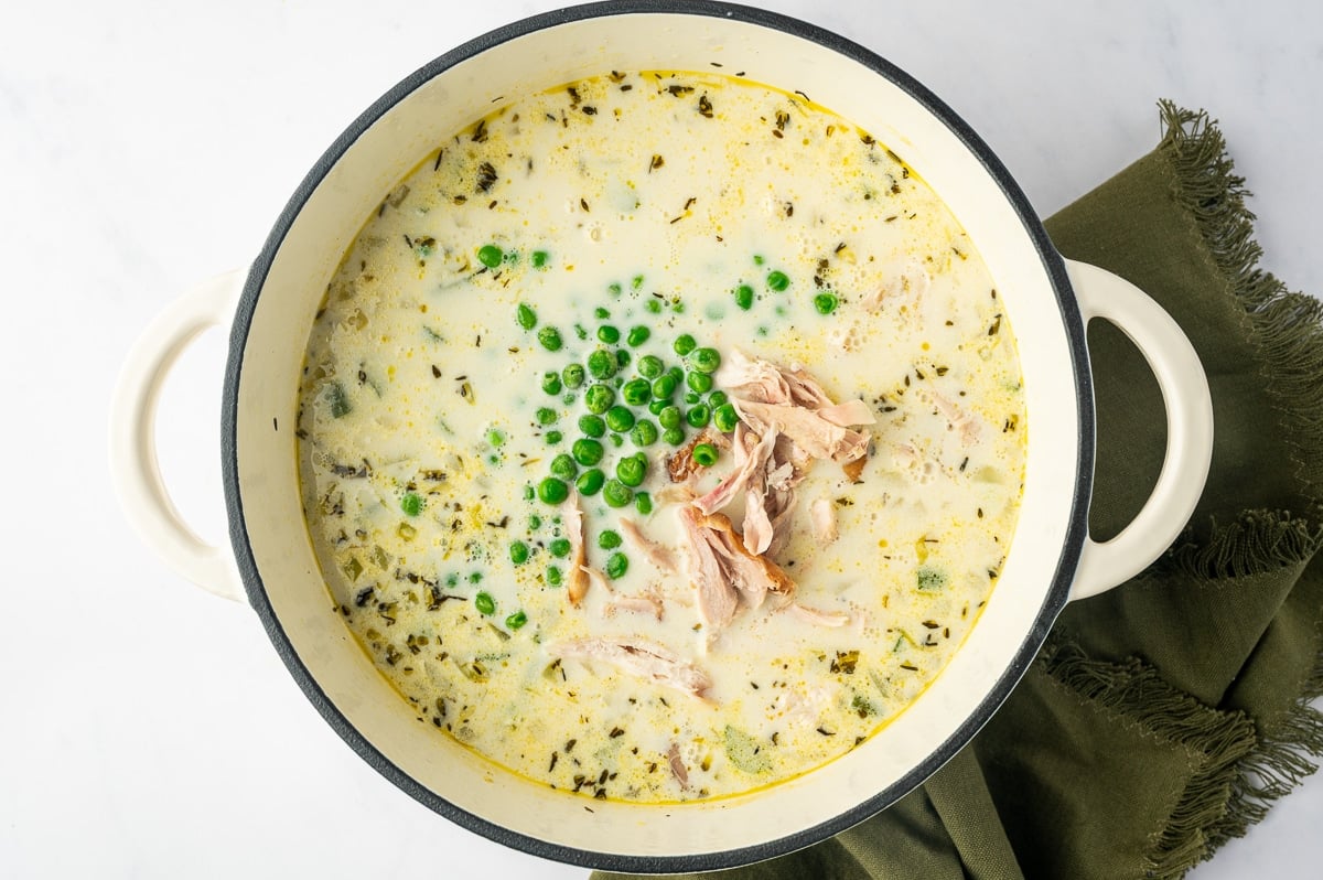 Shredded rotisserie chicken and bright green peas in a Dutch oven filled with creamy, thyme-seasoned chicken broth.