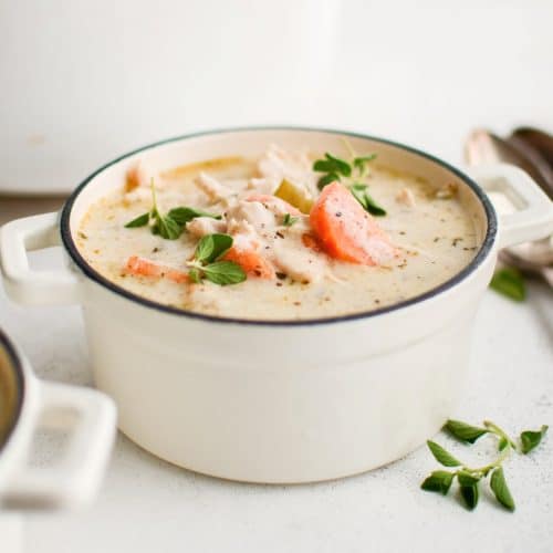 Small white soup bowl filled with creamy chicken soup garnished with fresh parsley and oregano.