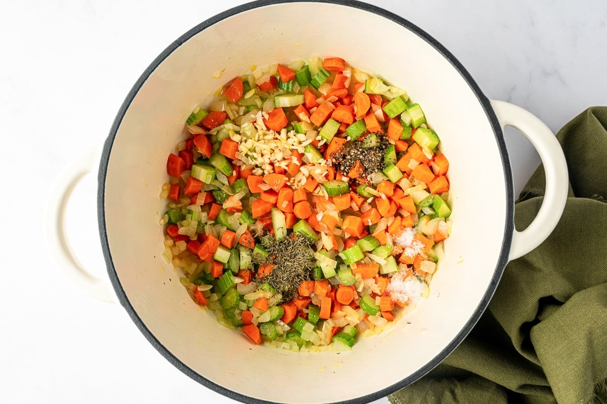 Minced garlic, dried thyme, salt, and black pepper added to sautéed carrots, celery, and onions in a Dutch oven.