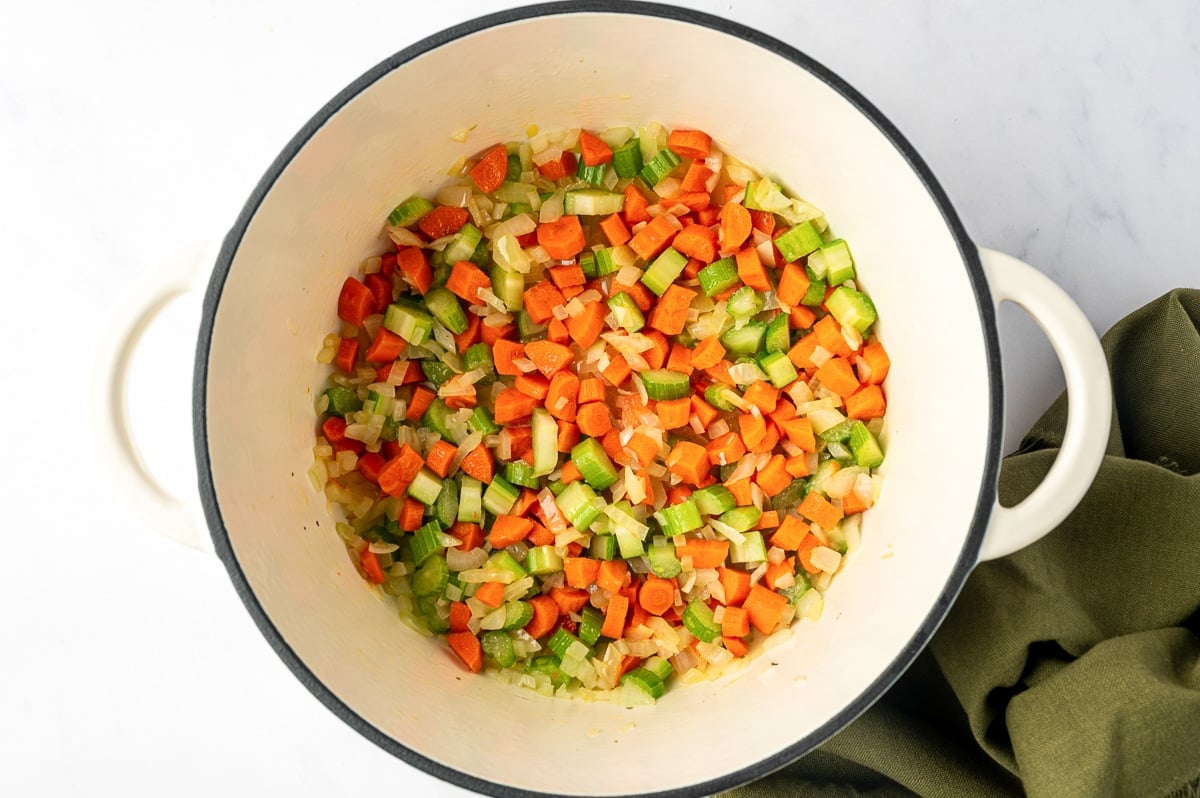Diced onions, carrots, and celery sautéing in butter in a white enameled Dutch oven.