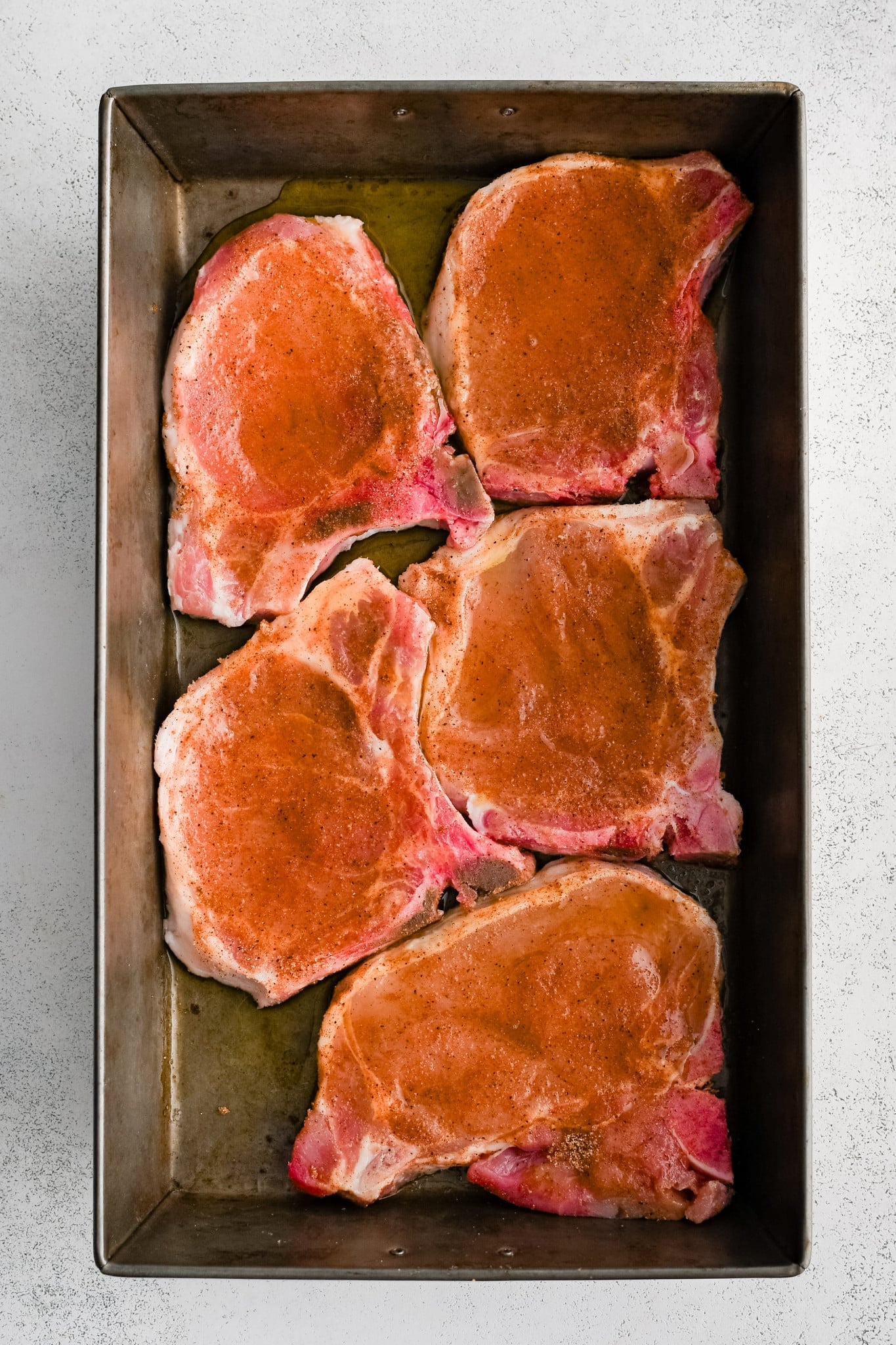 Five bone-in pork chops seasoned and drizzled with olive oil in a large baking dish.