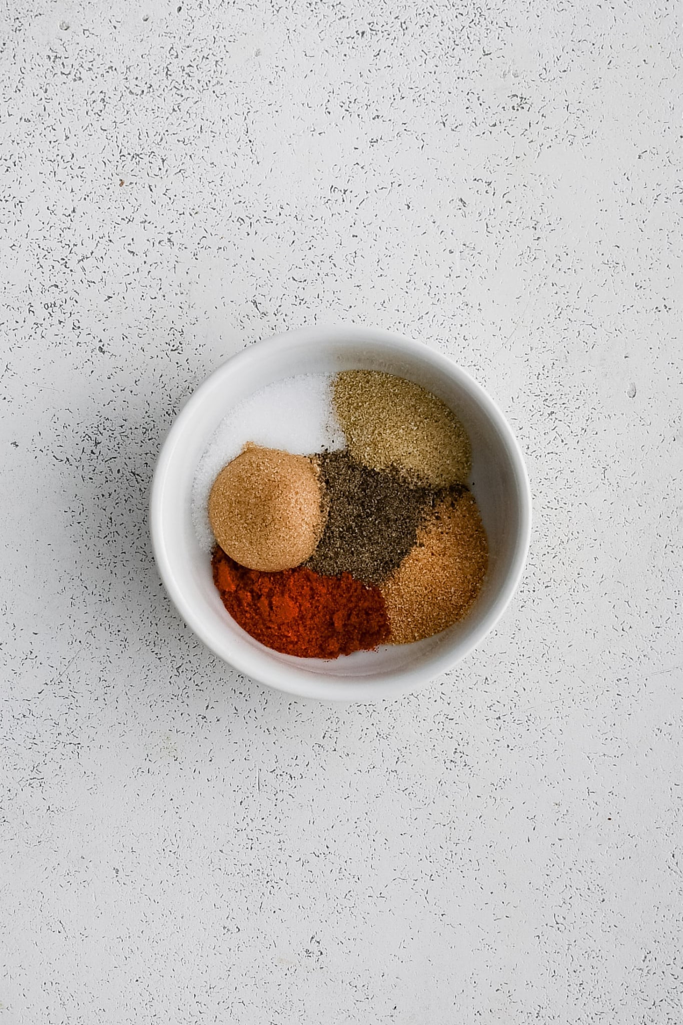 Small bowl filled with different seasoning needed to make dry rub for pork chops.