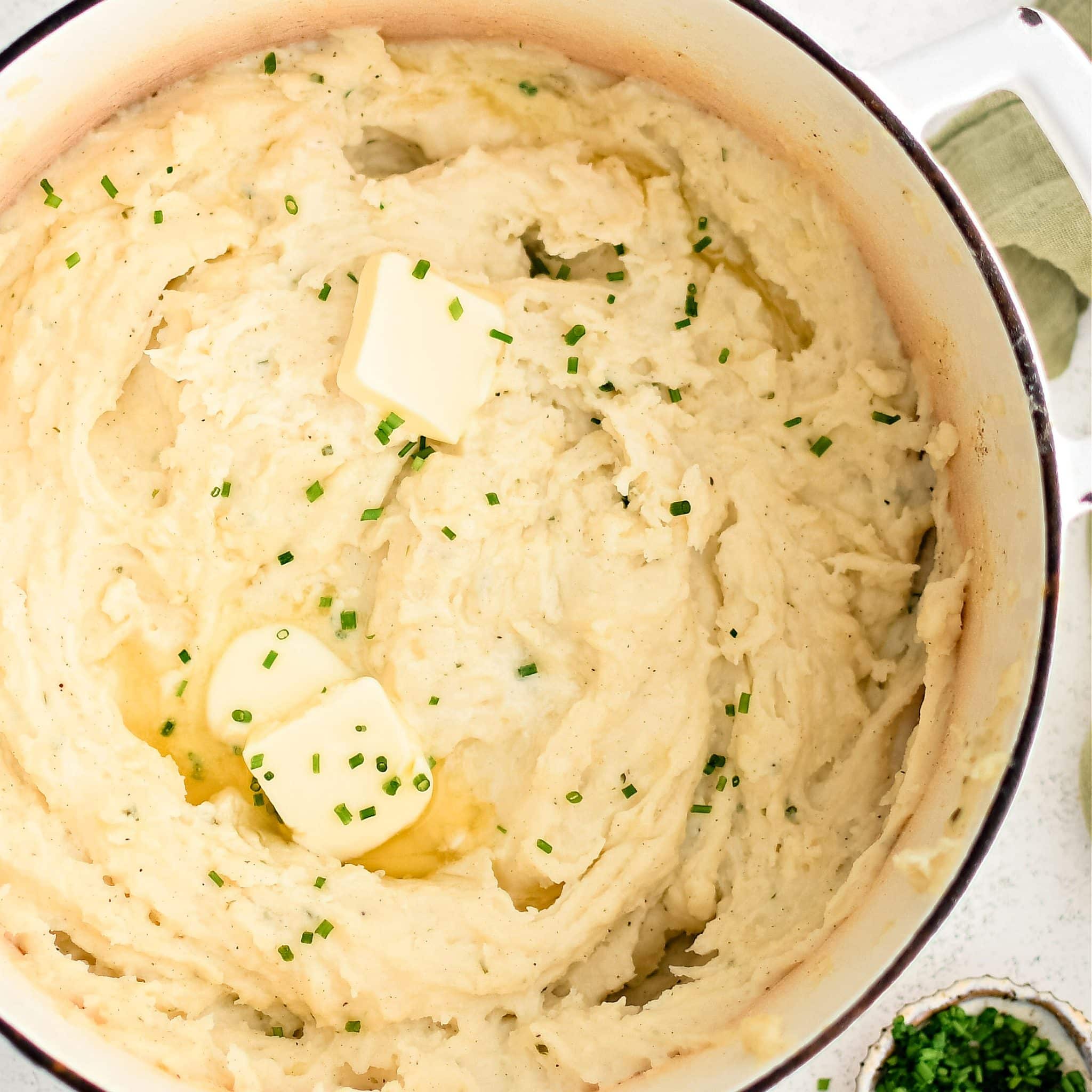 Large stock pot filled with creamy herb and garlic infused mashed potatoes topped with two pats of butter and freshly chopped chives.