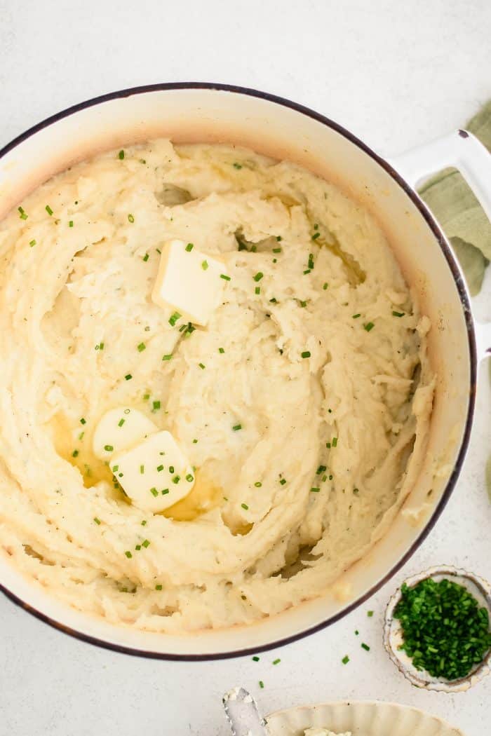 Large stock pot filled with creamy herb and garlic infused mashed potatoes topped with two pats of butter and freshly chopped chives.