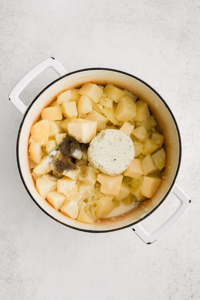 Large stock pot filled with tender boiled potatoes topped with butter, salt, black pepper, and boursin cheese.