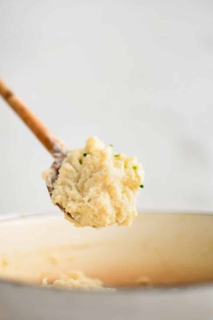 A generous serving of creamy Boursin mashed potatoes scooped from a large pot on an oversized metal spoon with a wood handle.