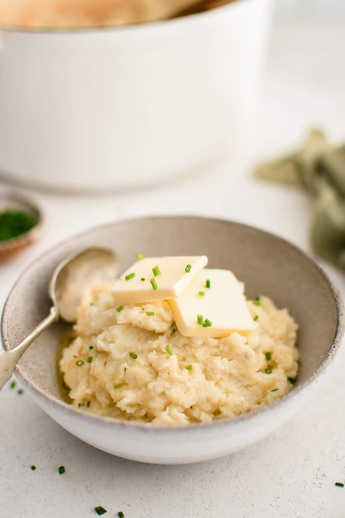 Ceramic serving bowl filled with creamy mashed potatoes seasoned with butter, cream, and Boursin cheese, and topped with butter and fresh chives.