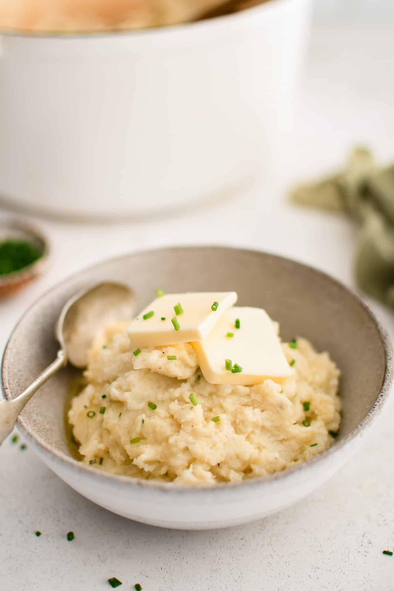 Ceramic serving bowl filled with creamy mashed potatoes seasoned with butter, cream, and Boursin cheese, and topped with butter and fresh chives.