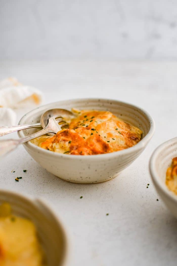 Shallow serving bowl filled with a large serving of thinly sliced scalloped potato casserole in a homemade cream sauce and topped with golden baked cheese.