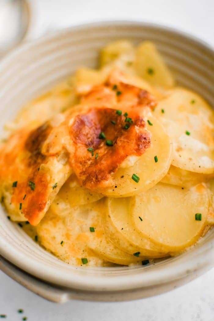 Shallow serving bowl filled with a large serving of thinly sliced scalloped potato casserole in a homemade cream sauce and topped with golden baked cheese.