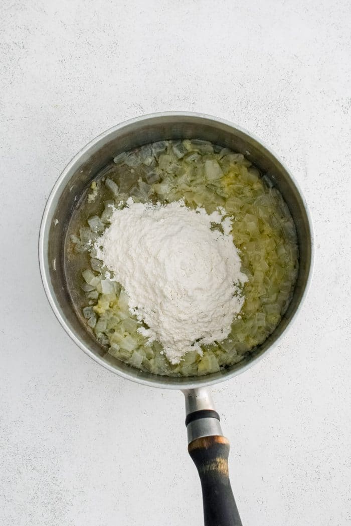 All purpose flour added to a medium saucepan filled with buttery sauteed onions with garlic.