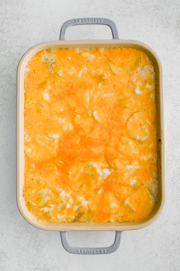 Large 9x13-inch baking dish filled with partially baked cheesy scalloped potatoes.