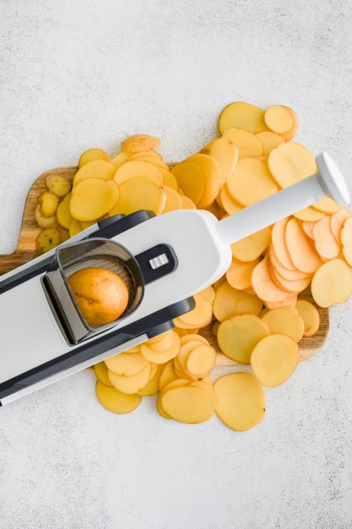 Mandoline slicer thinly slicing Yukon Gold potatoes.