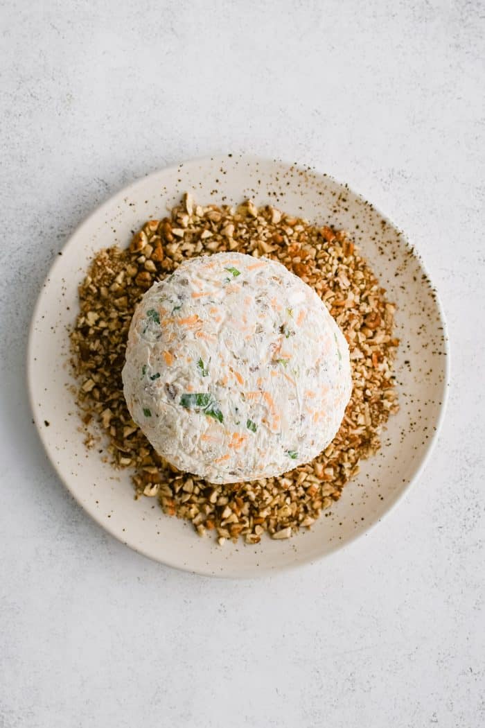 Refrigerated cheese ball on a plate filled with crushed pecans.