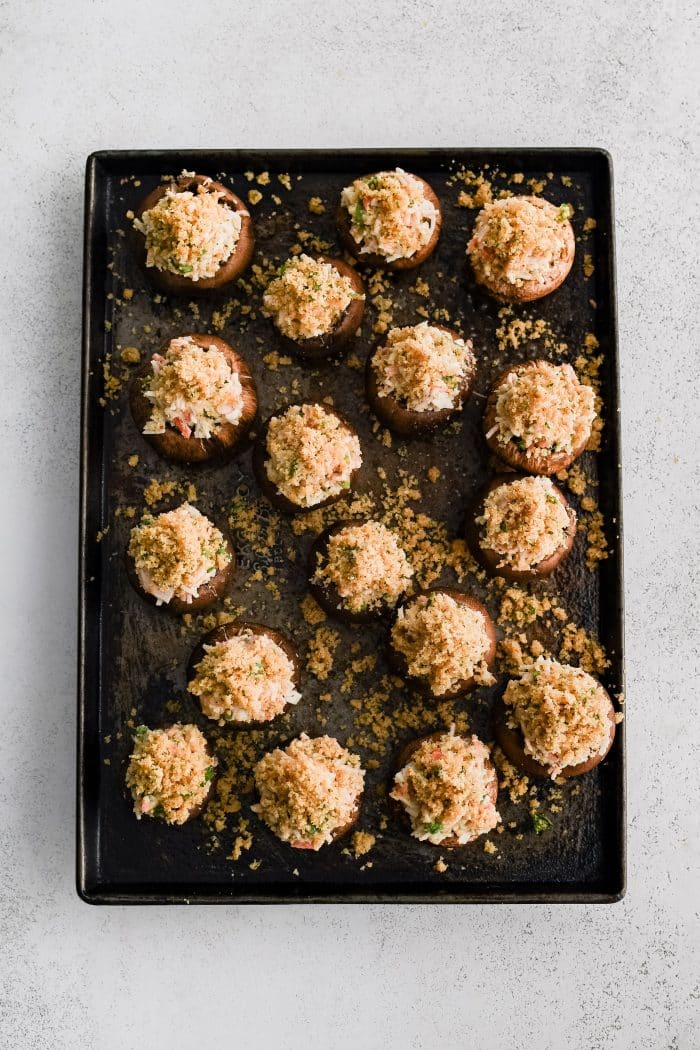 Large baking sheet filled with fourteen mushroom caps stuffed with creamy crab mixture and sprinkled with a buttery breadcrumb topping.