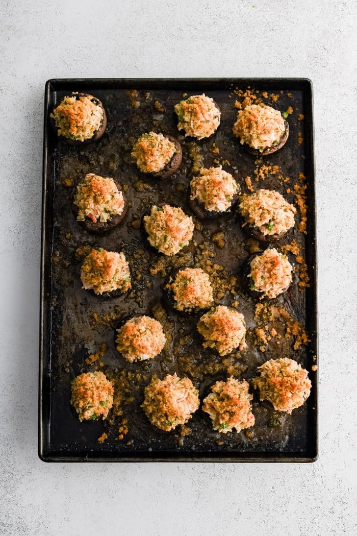 Large baking sheet filled with fourteen creamy crab stuffed mushrooms with a golden crispy breadcrumb topping.