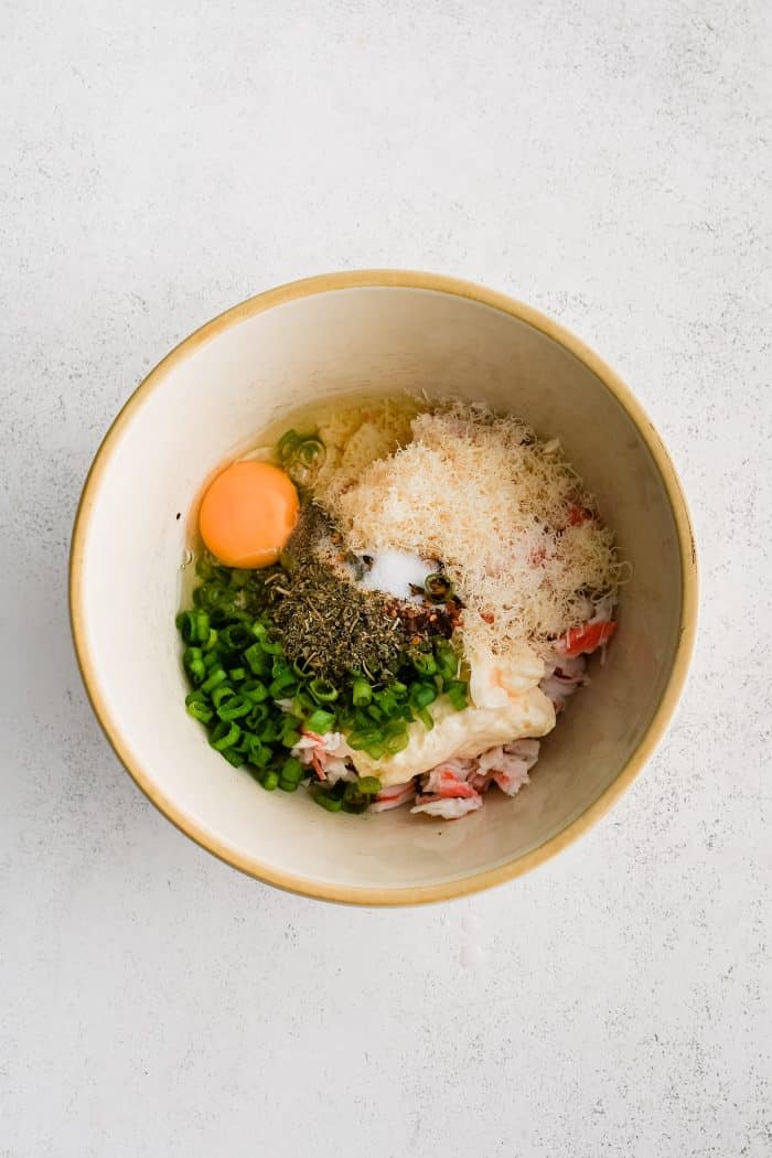 Medium mixing bowl filled with three tablespoons of melted butter, chopped green onions, five tablespoons of breadcrumbs, grated Parmesan cheese, mayonnaise, egg, dried Italian seasoning, garlic powder, salt, and red chili flakes.