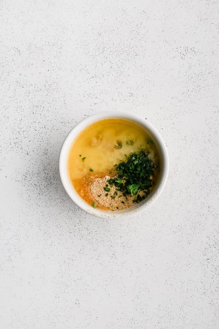 Small white bowl filled with melted butter, bread crumbs, and fresh parsley.