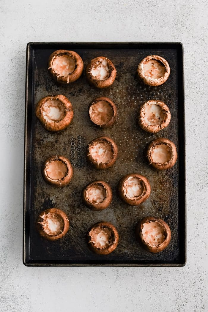 Large baking sheet filled with fourteen prepared mushroom caps stem-side up.