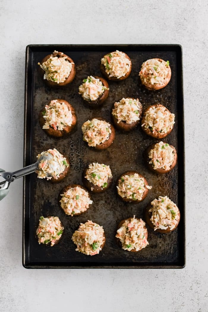 Large baking sheet filled with fourteen mushroom caps stuffed with creamy crab mixture.