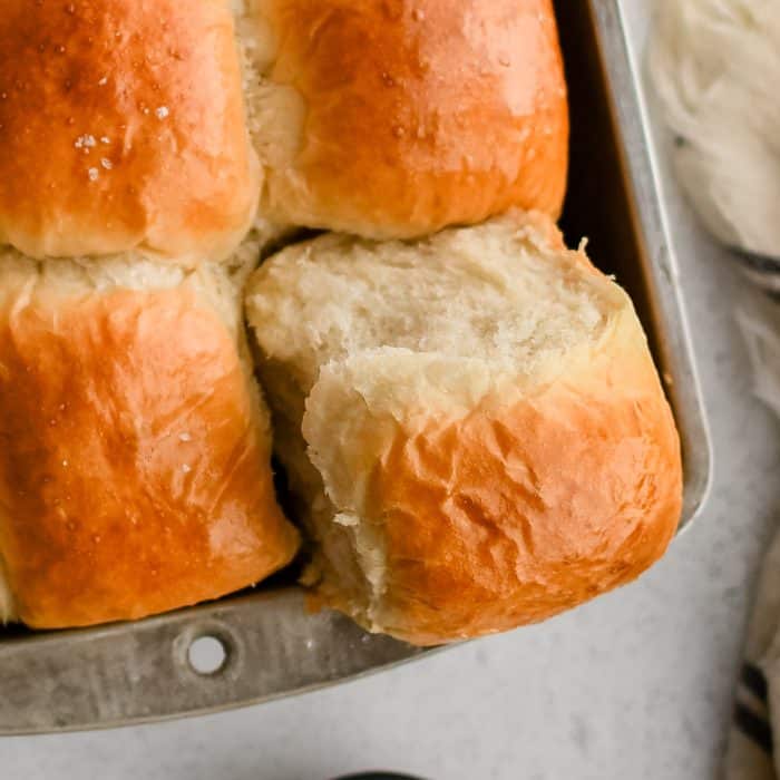 One corner dinner roll removed partially from a pan filled with perfectly baked yeast dinner rolls with golden tops.