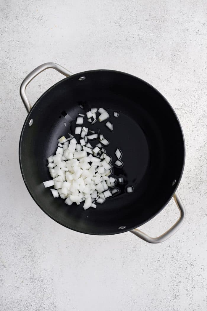 Chopped white onion being sautéed in olive oil in a large black pot.