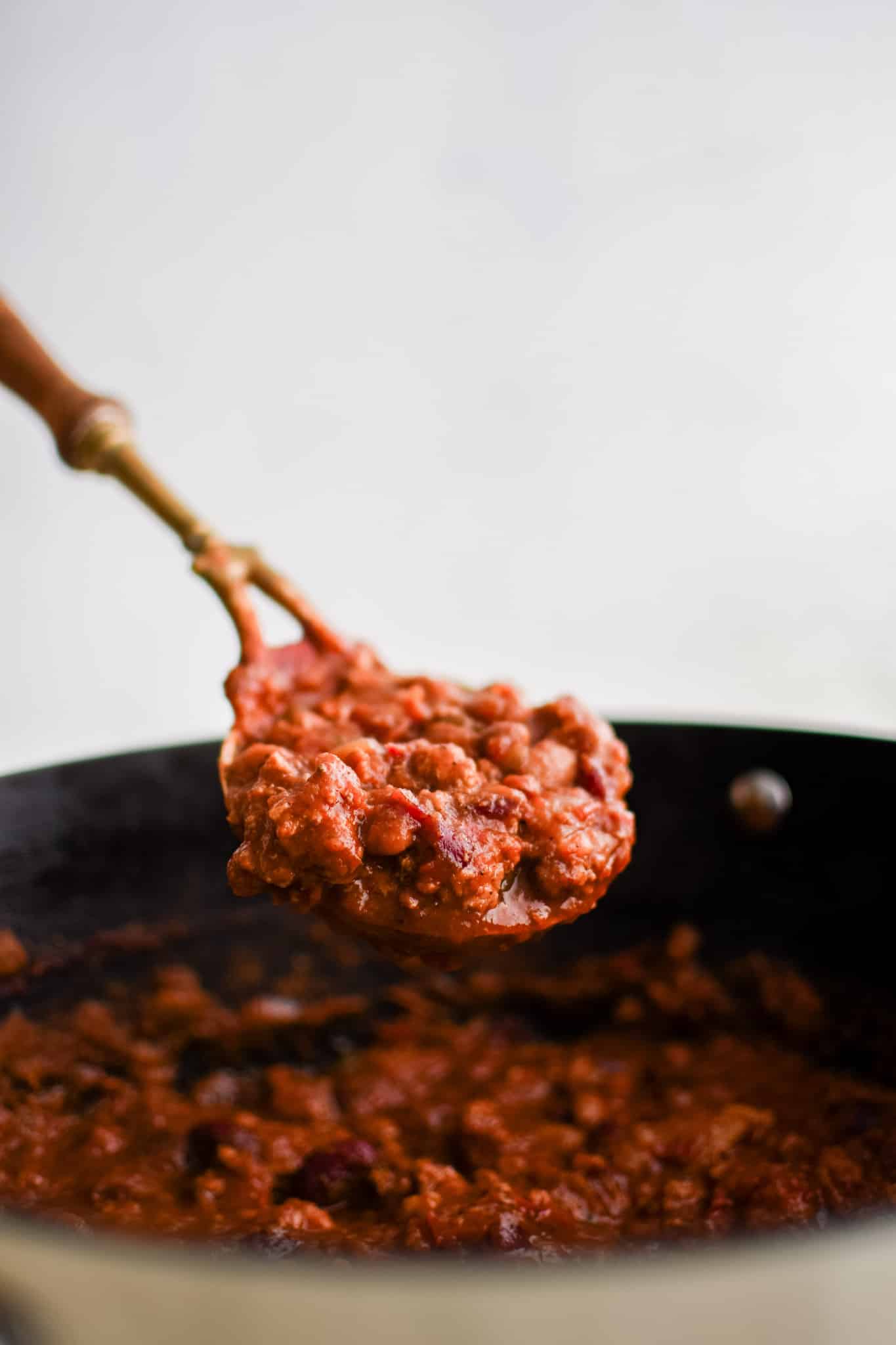 Large serving spoon hovering over a large pot each filled with homemade turkey chili.