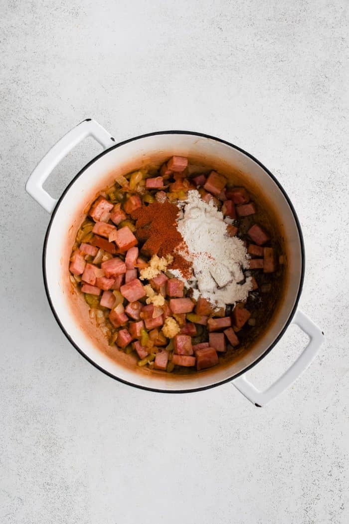 All-purpose flour, paprika, minced garlic, and pepper added to a large pot filled with diced ham and softened onions and celery.