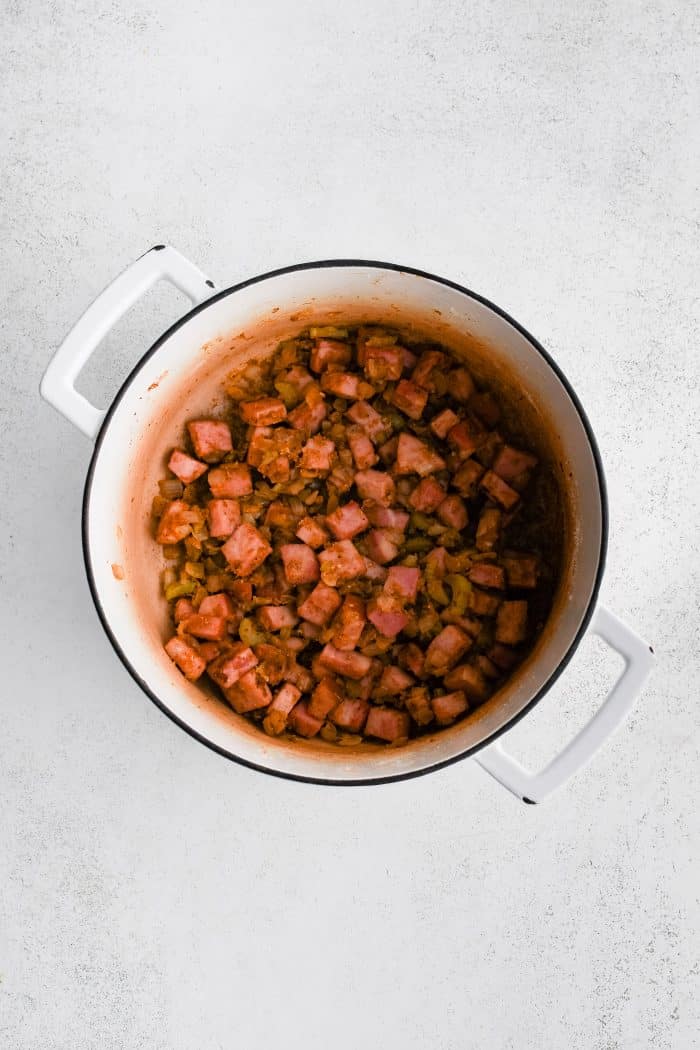 Softened celery and onions with chunks of ham coated in roux and seasoning in a large pot.