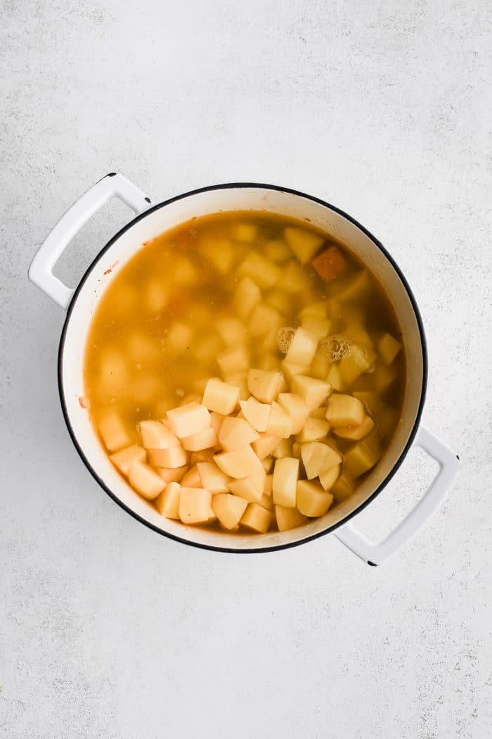 Chicken broth and chopped potatoes added to a large pot filled with softened celery and onions with chunks of ham coated in roux and seasoning.