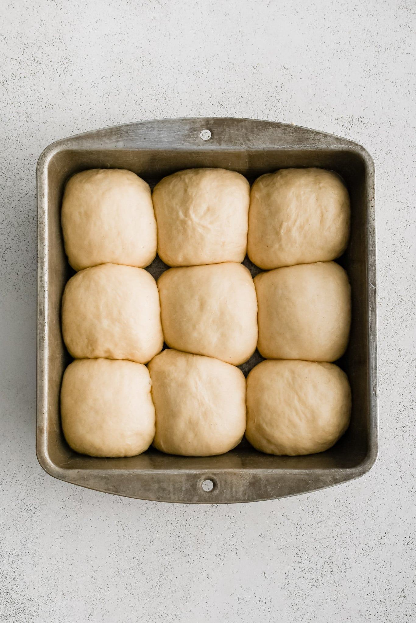 A greased 9x9-inch baking pan filled with 9 shaped dough balls before the second rise.