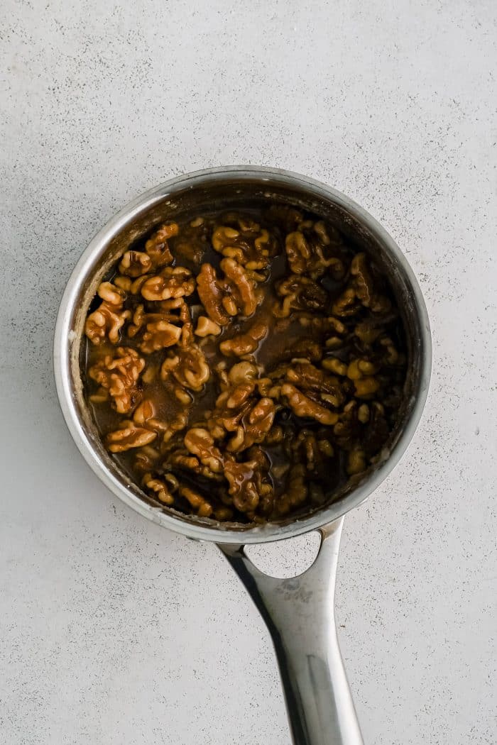 Walnut pieces in a saucepan filled with thickened syrup of water, sugar, and lemon juice.