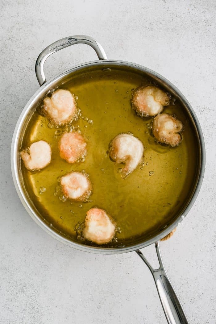 Stainless steel skillet filled with hot cooking oil and 8 frying shrimp coated in a light batter.