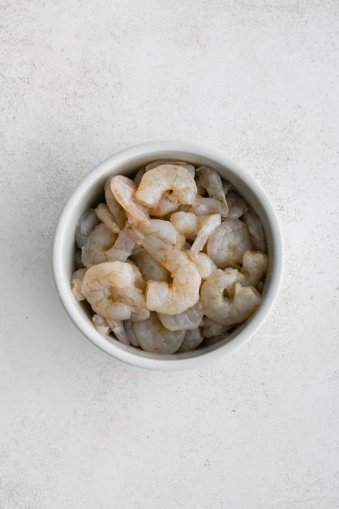 Bowl filled with large peeled and deveined raw shrimp.