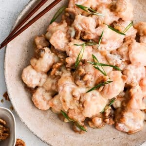 Large round plate filled with homemade honey walnut shrimp garnished with sliced green onions.