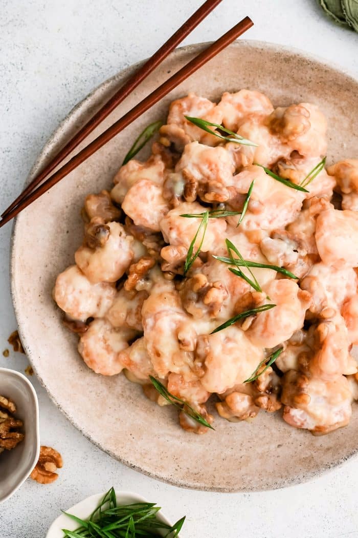 Large round plate filled with copycat panda express honey walnut shrimp garnished with sliced green onions.