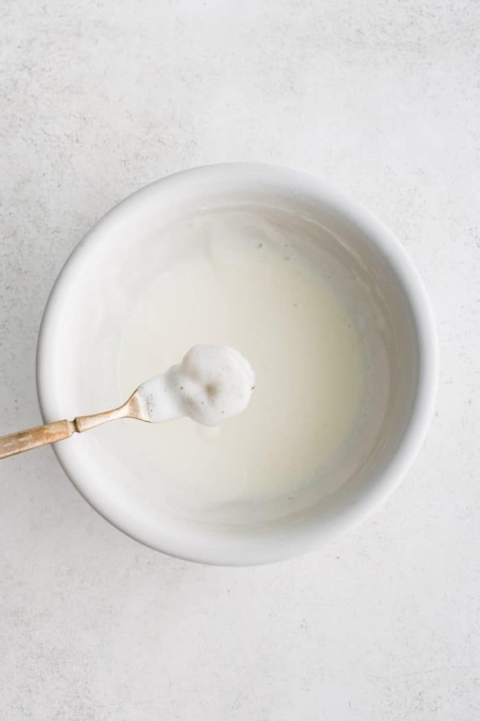 A single shrimp being dipped into a bowl filled with a white frying batter made from egg whites, club soda, and tapioca flour.