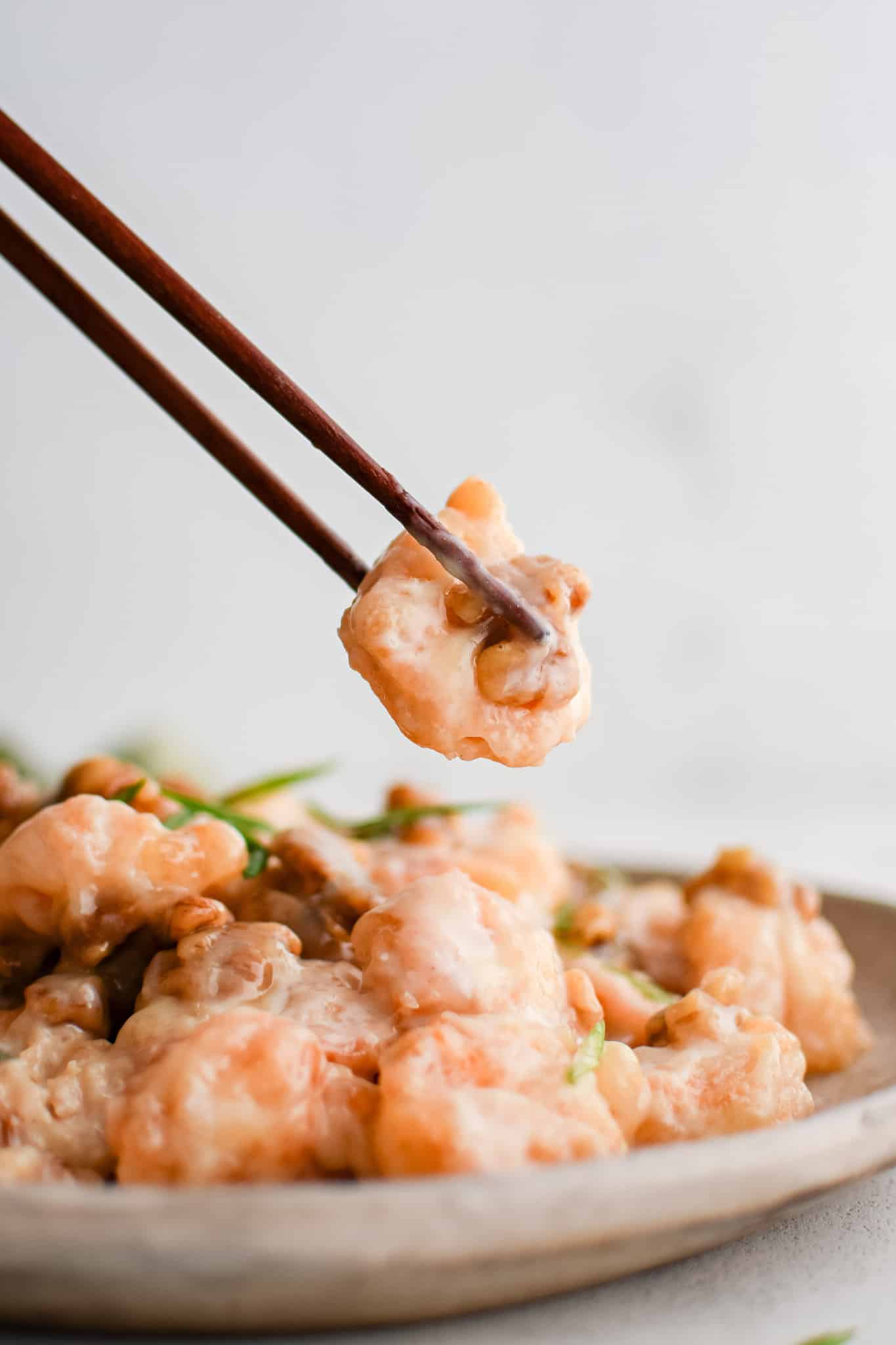 Chopsticks picking up a single piece of shrimp and piece of candied walnut coated in sweet mayonnaise based sauce for the perfect bite of honey walnut shrimp.