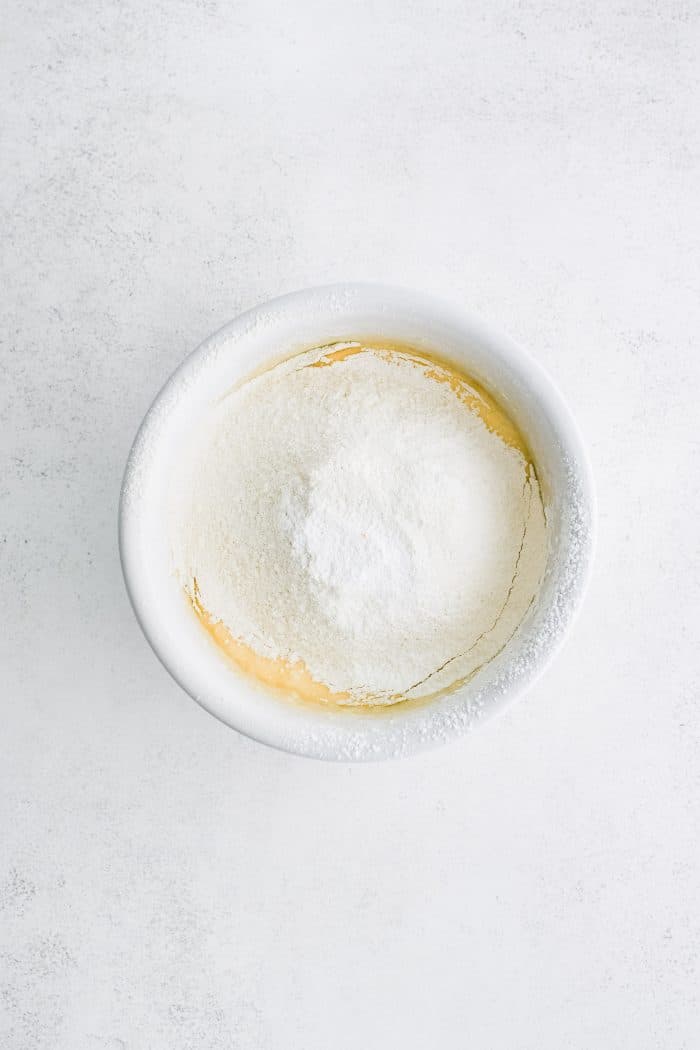 Sifted flour mixture added to a large white mixing bowl filled with the wet ingredients for vanilla cake.