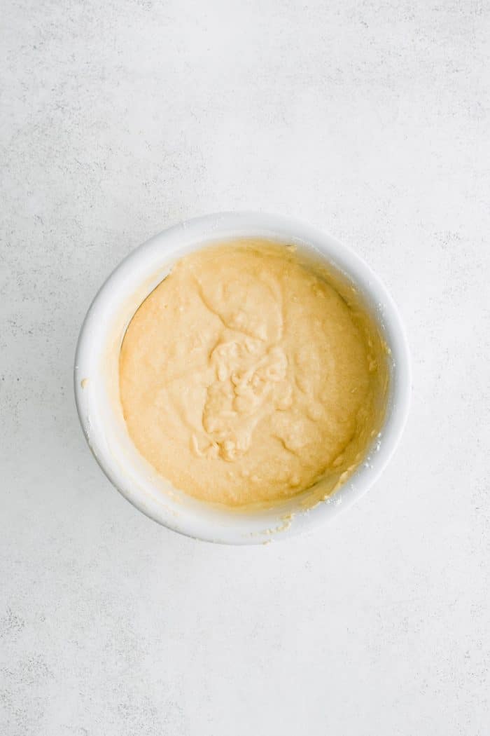 Large white mixing bowl filled with prepared vanilla cake batter.