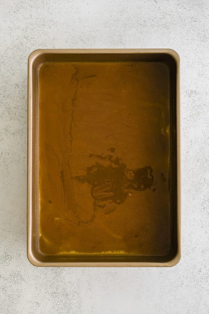 A 9x13 inch baking pan filled with melted butter mixed with brown sugar.