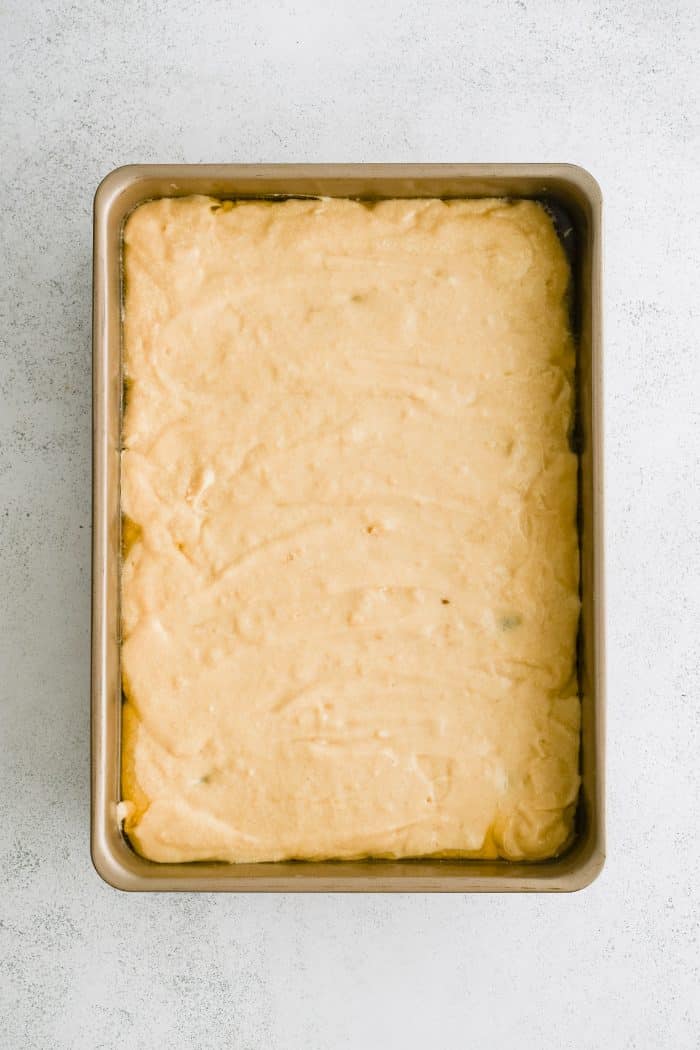 Vanilla cake batter poured into a 9x13 inch baking pan filled with a bottom layer of melted butter mixed with brown sugar and rows of pineapple rings with maraschino cherries in the middle.