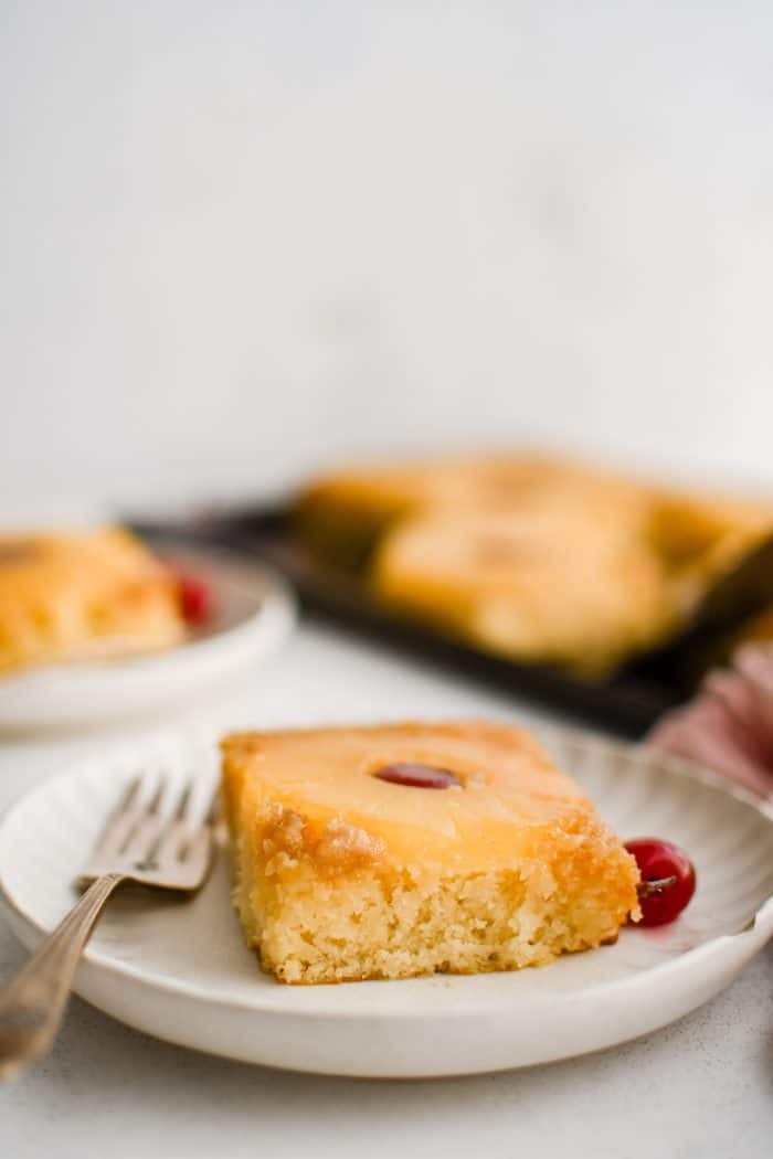 Small white serving plate with a single square slice of pineapple upside down cake.