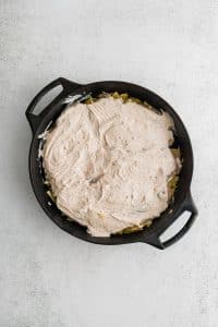 Large cast iron skillet filled with crushed potato chips topped with thinly sliced raw chicken breasts smothered in s seasoned mixture of sour cream.