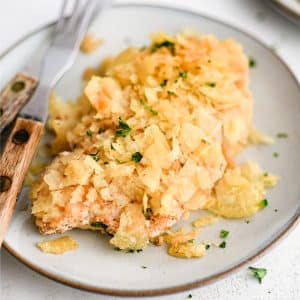 Serving plate with a thinly sliced baked chicken breast that's been coated in seasoned sour cream and crushed potato chips.