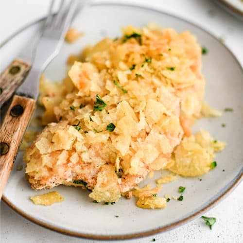 Serving plate with a thinly sliced baked chicken breast that's been coated in seasoned sour cream and crushed potato chips.