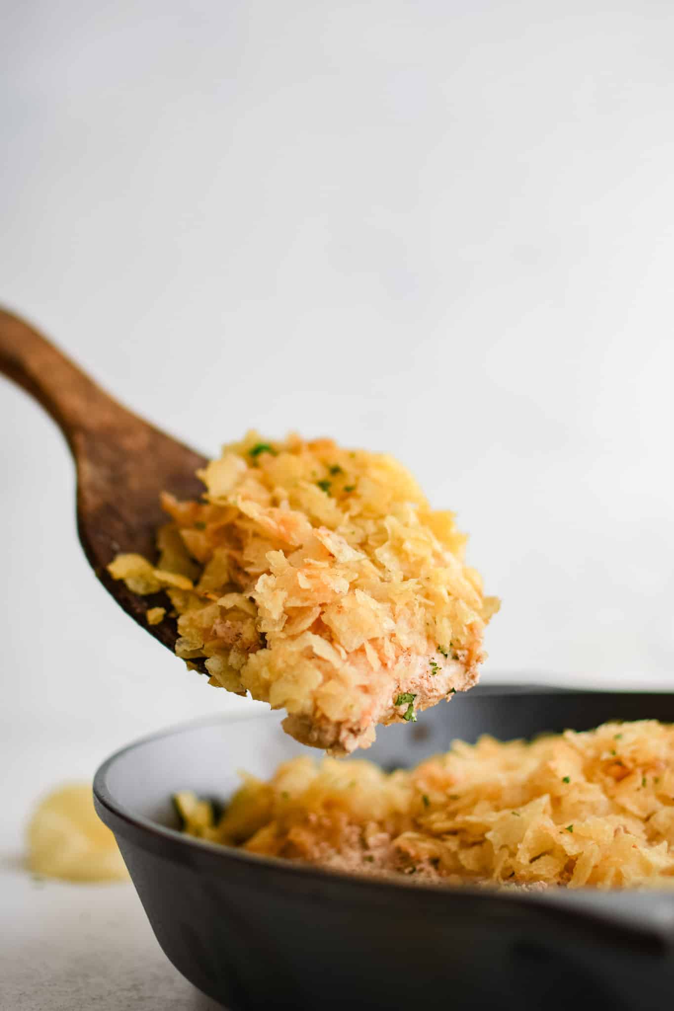 A piece of oven baked potato chip chicken being removed from a large cast iron skillet.