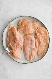 Fork piercing four thinly sliced chicken breasts.