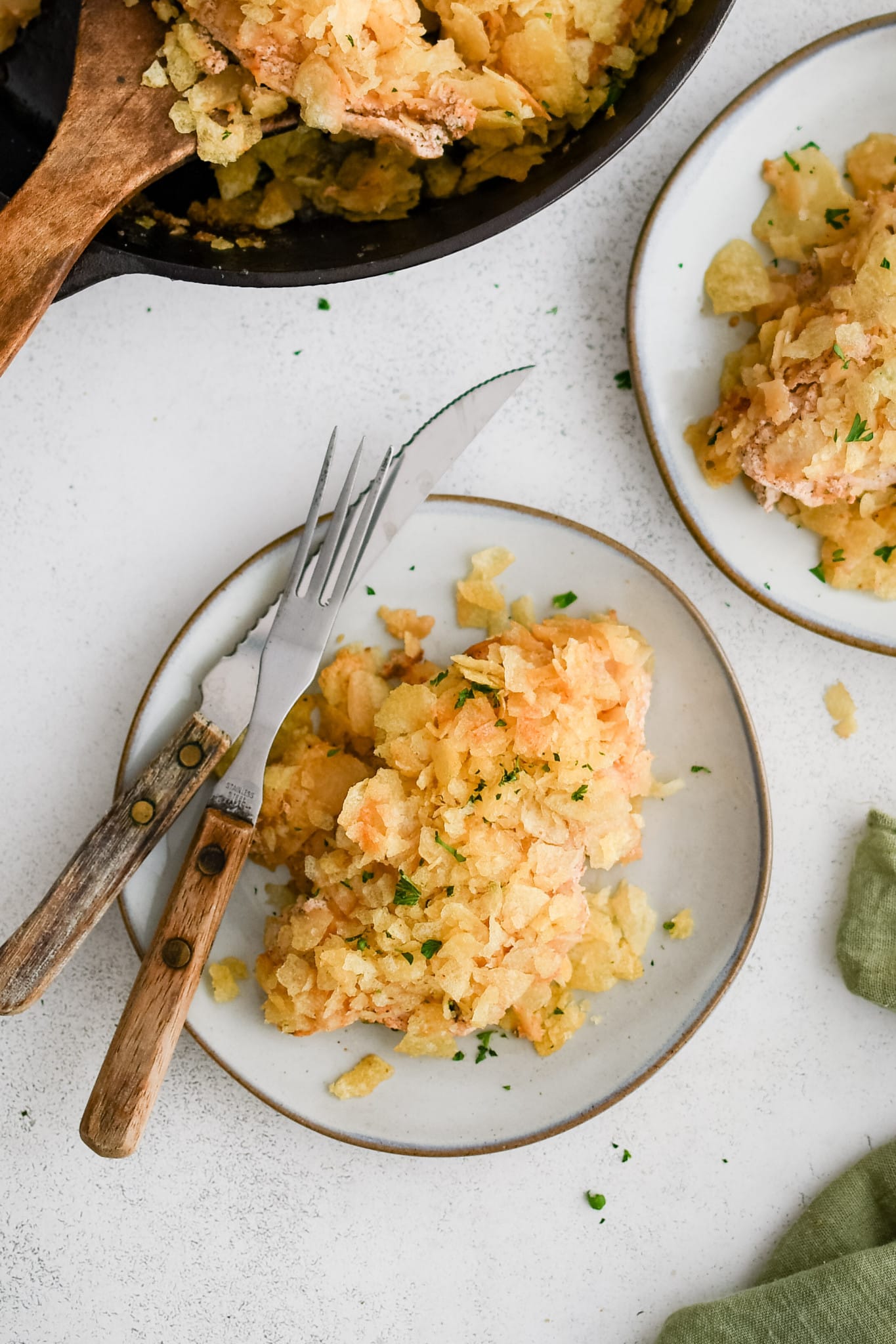 Two serving plates each with a thinly sliced baked chicken breast that's been coated in seasoned sour cream and crushed potato chips.