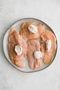 A dollop of seasoned sour cream mixture on four uncooked thinly sliced chicken breasts.